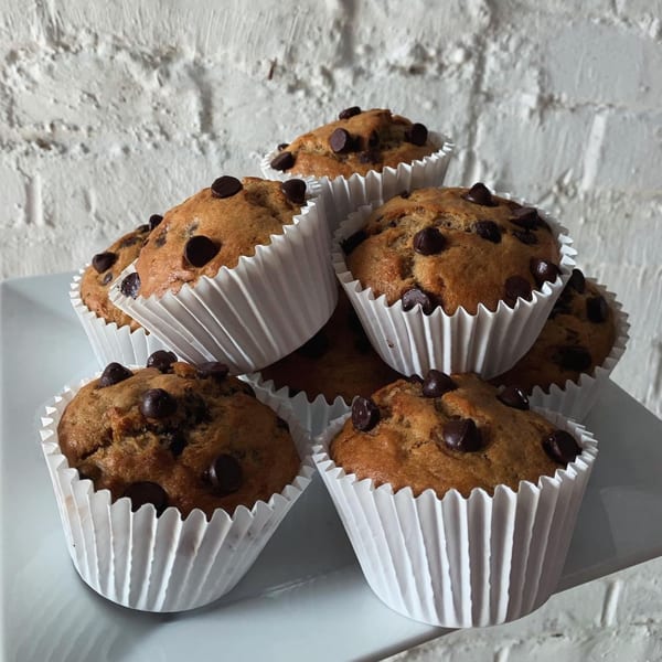 A pile of vegan chocolate chip muffins in white paper liners on a white plate.