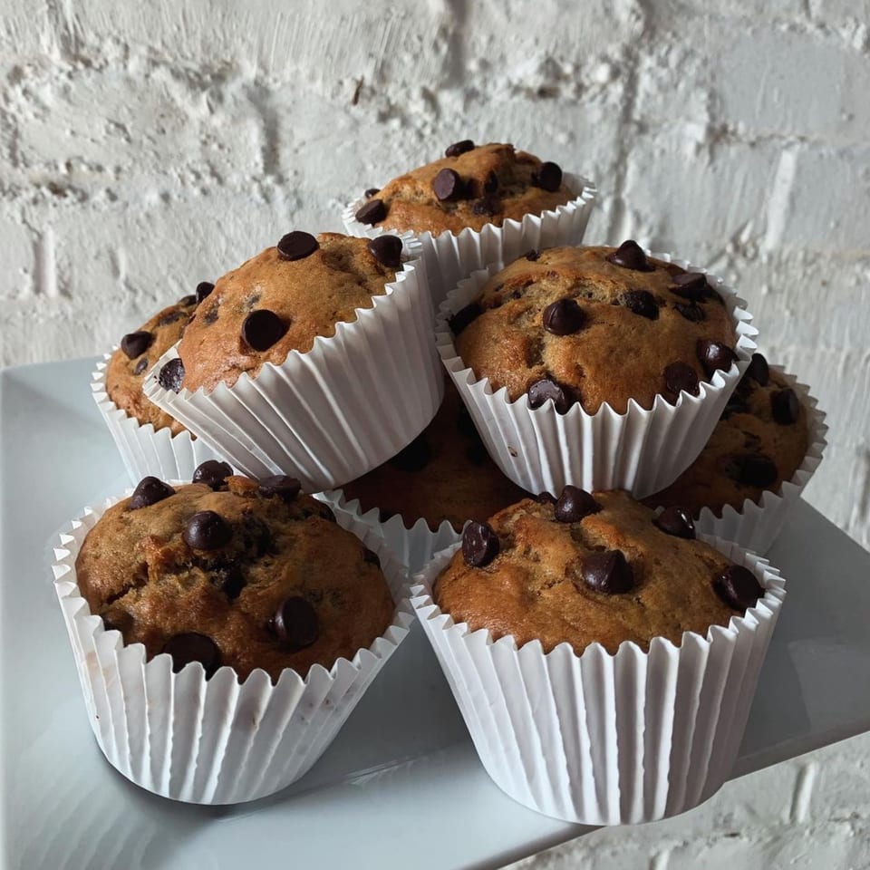 A pile of vegan chocolate chip muffins in white paper liners on a white plate.