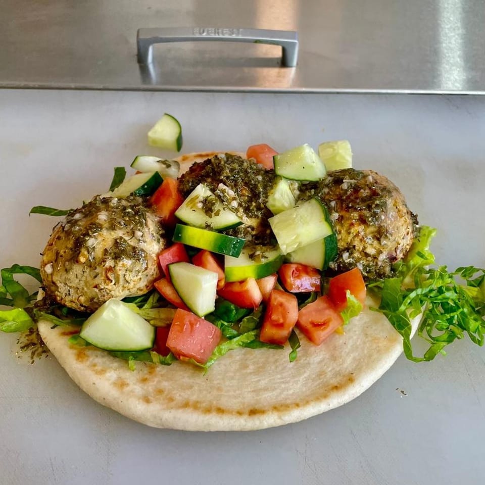 Vegan falafel pita with lettuce, diced tomatoes, and cucumbers, drizzled with sauce.
