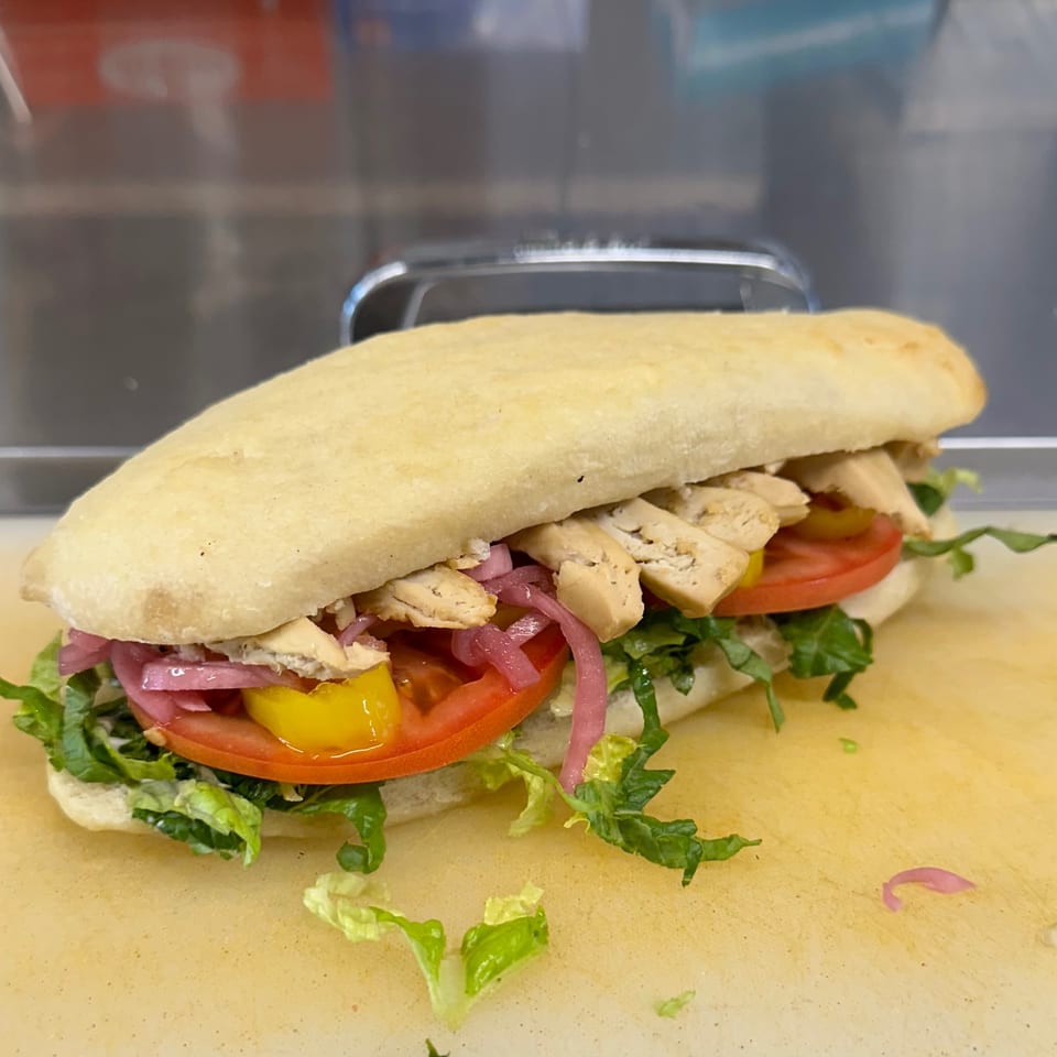 A vegan sandwich with plant-based chicken, lettuce, tomatoes, pickled onions, and yellow peppers.