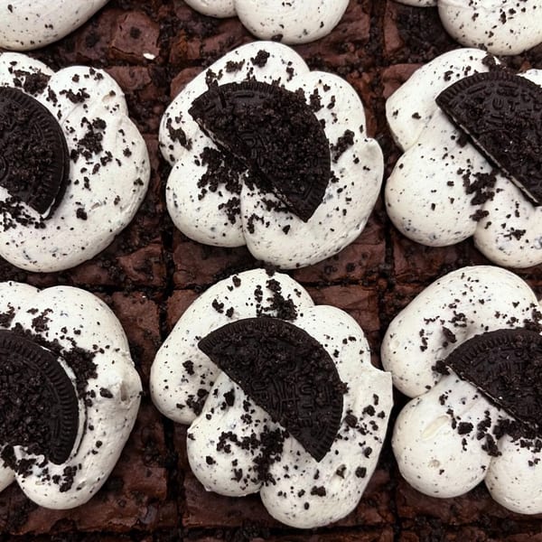 Close-up of vegan brownies topped with white cream and crushed chocolate cookies.
