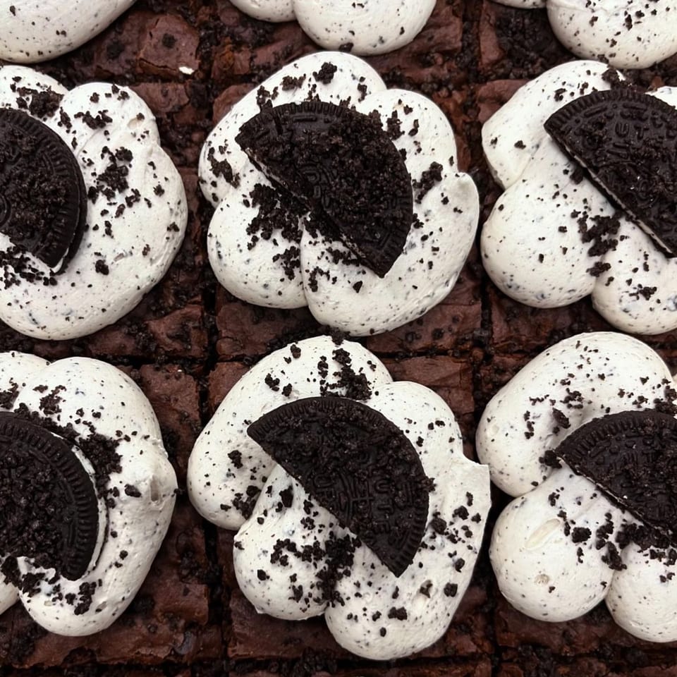 Close-up of vegan brownies topped with white cream and crushed chocolate cookies.