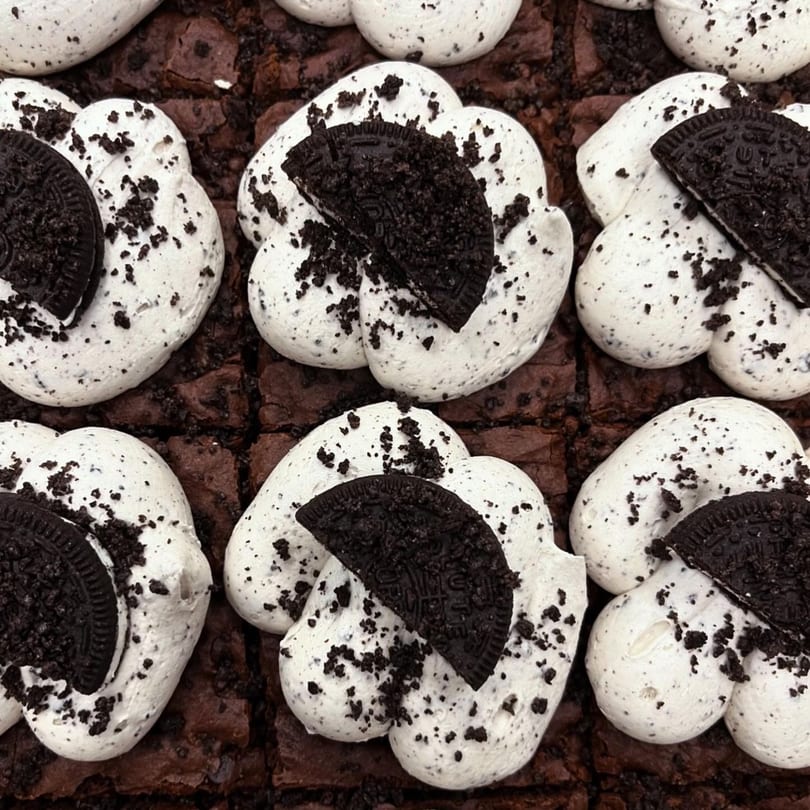 Close-up of vegan brownies topped with white cream and crushed chocolate cookies.
