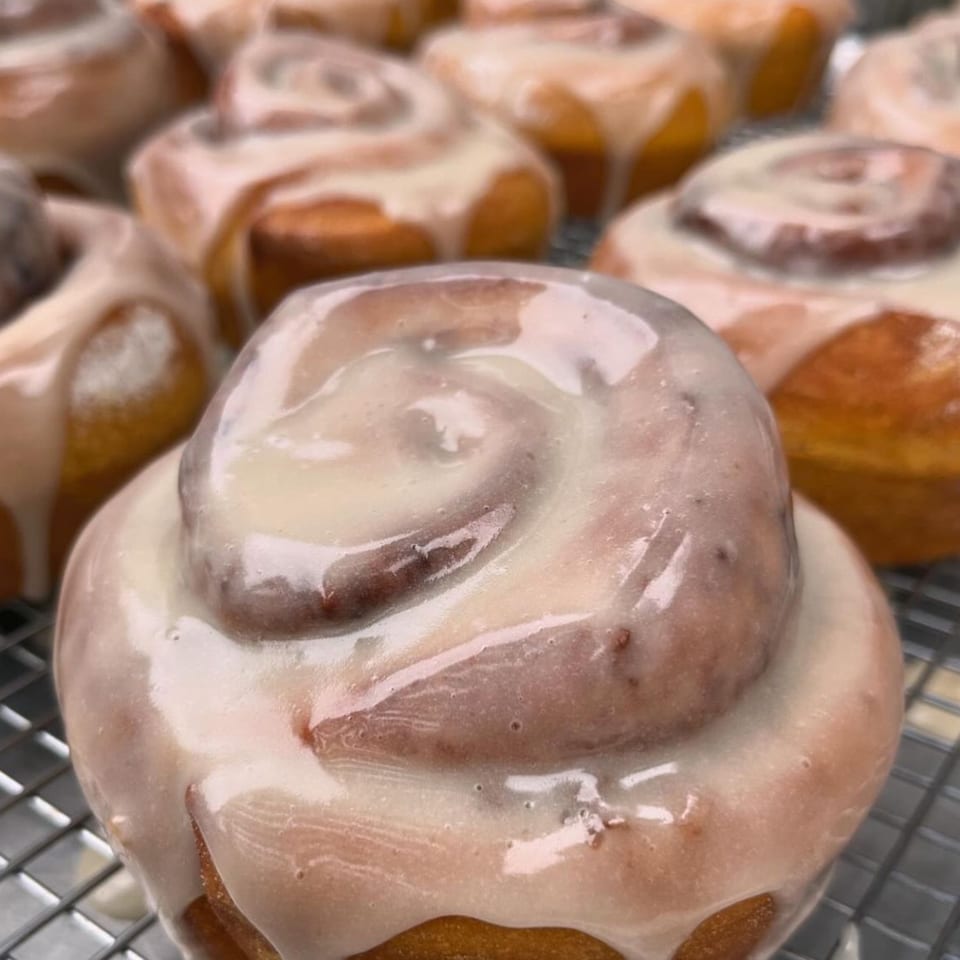 Close-up of a freshly baked, vegan cinnamon roll with white icing, on a cooling rack.