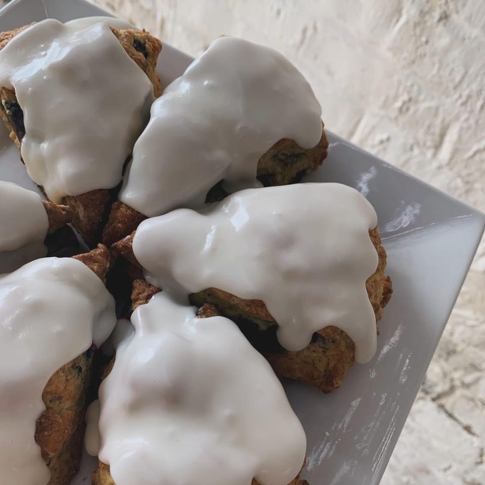 Close-up of several vegan scones with white icing on a white rectangular plate.