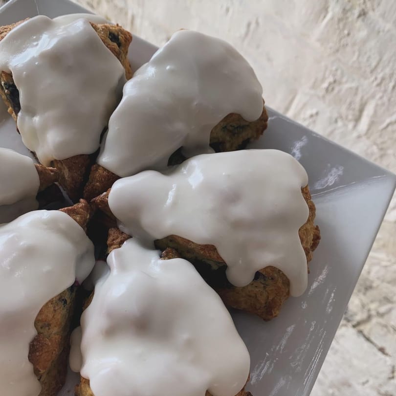 Close-up of several vegan scones with white icing on a white rectangular plate.