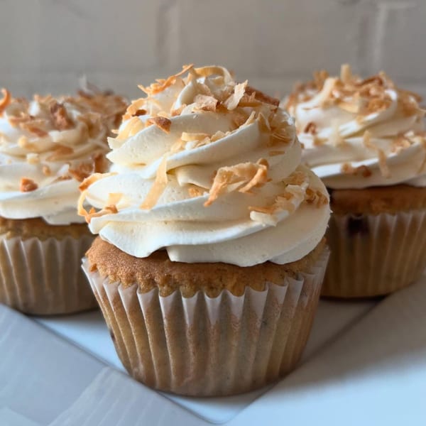 Three vegan cupcakes with white frosting and toasted coconut flakes on a white plate.