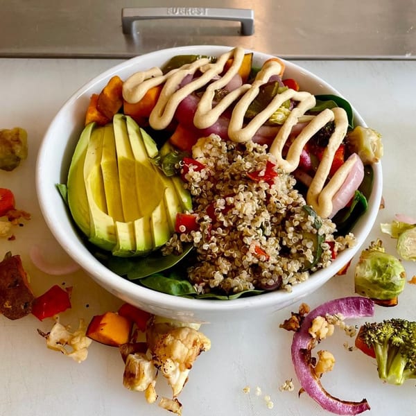 A vibrant vegan power bowl with quinoa, avocado, roasted vegetables, and a creamy drizzle.