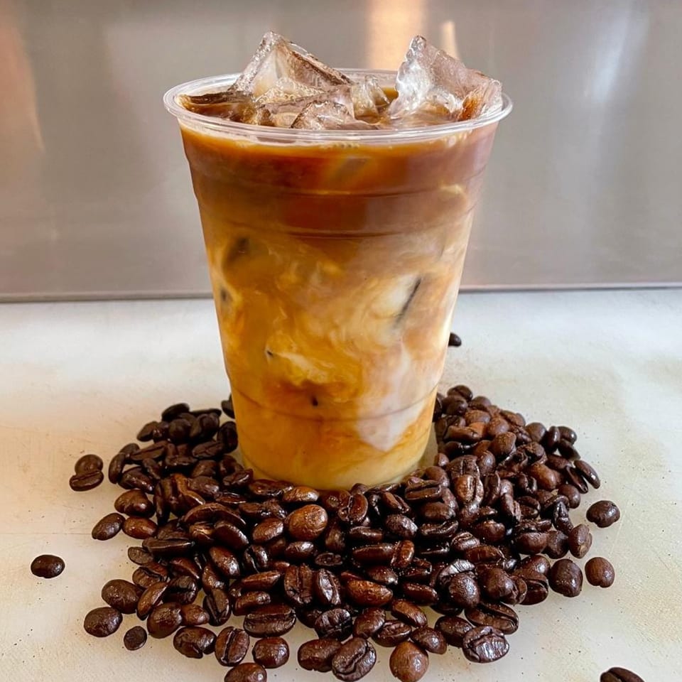 Iced coffee in a clear cup with ice and cream, surrounded by roasted coffee beans.