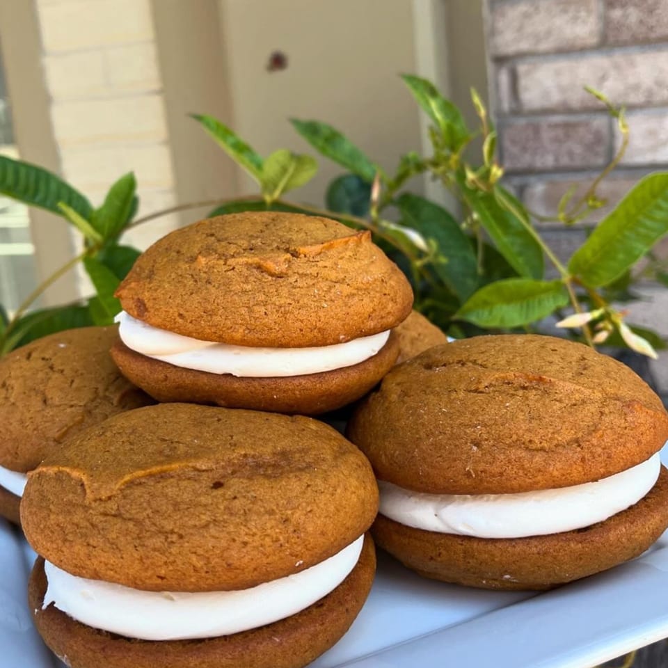 Several vegan whoopie pies with light brown cookies and white cream filling on a white plate.