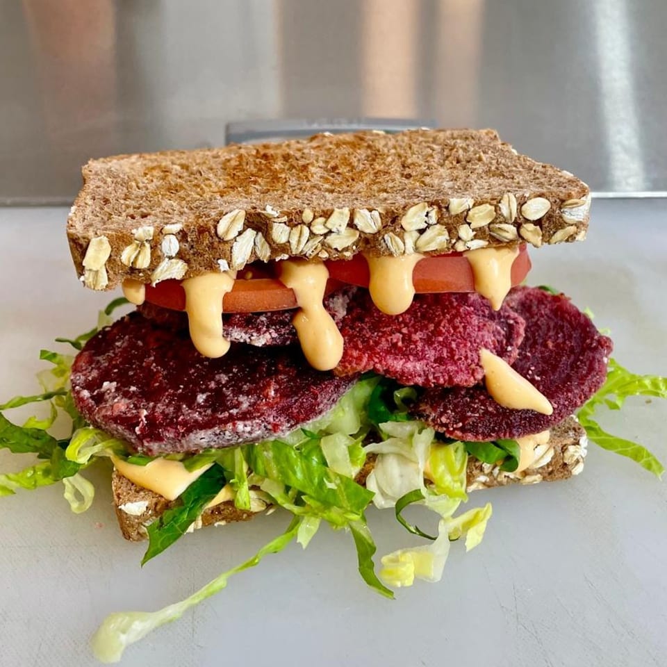 Vegan sandwich with beet patties, lettuce, tomato, and creamy sauce on oat-topped whole wheat bread.