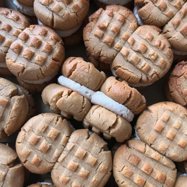 Close-up of vegan peanut butter sandwich cookies with white cream filling, some with a waffle pattern.