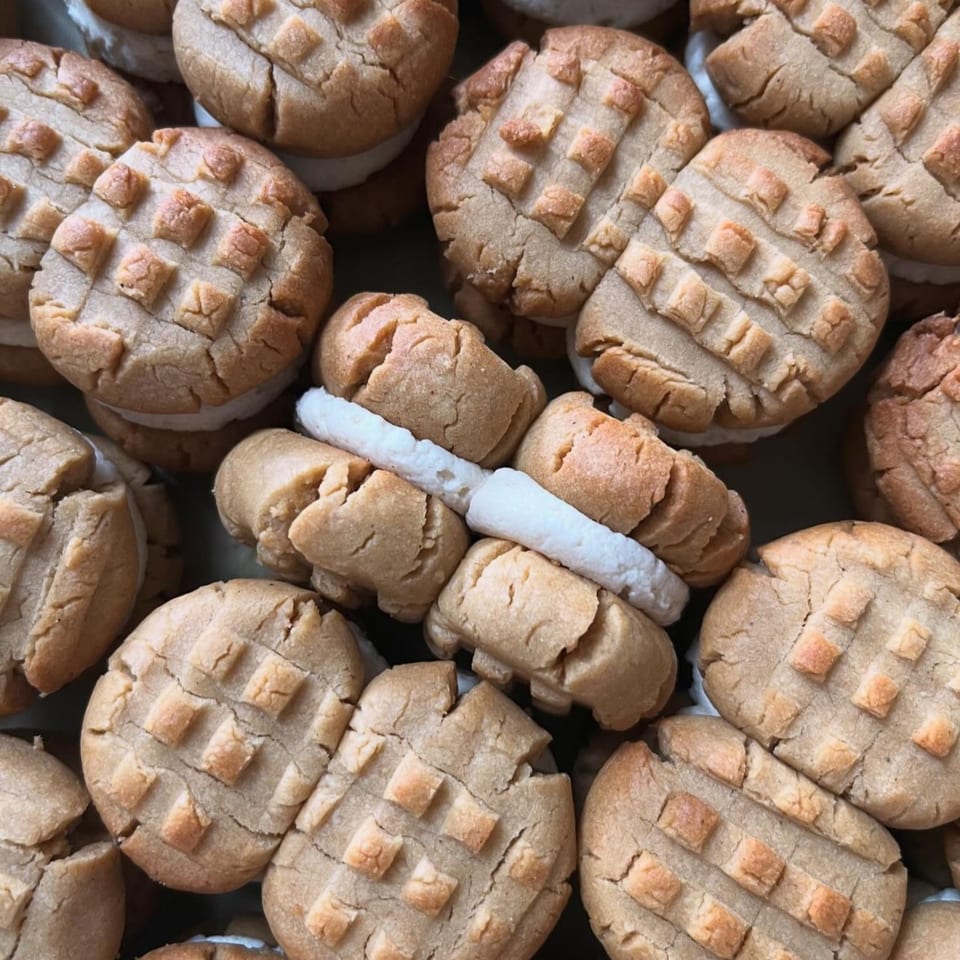 Close-up of vegan peanut butter sandwich cookies with white cream filling, some with a waffle pattern.