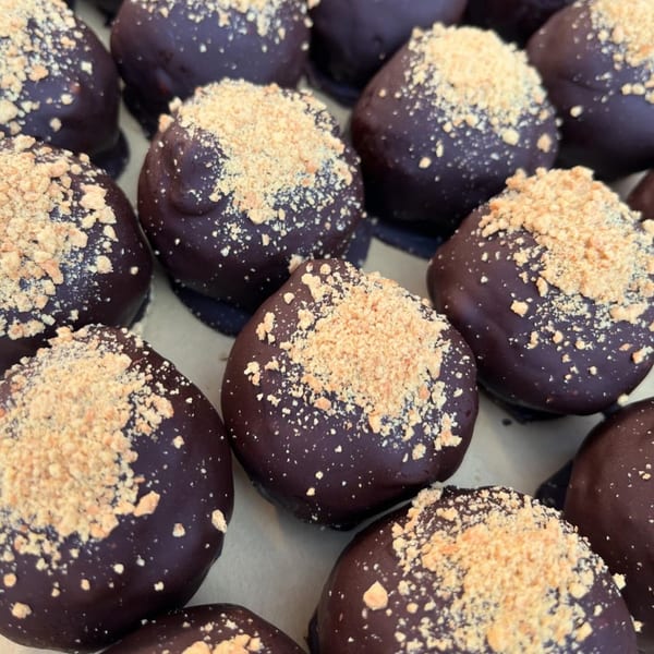 Close-up of vegan chocolate-covered PB+J truffles, topped with crushed peanuts.