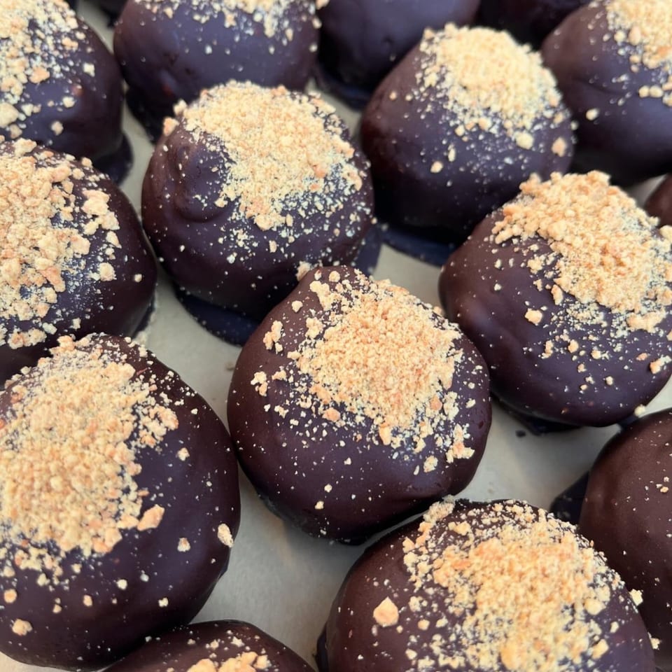 Close-up of vegan chocolate-covered PB+J truffles, topped with crushed peanuts.