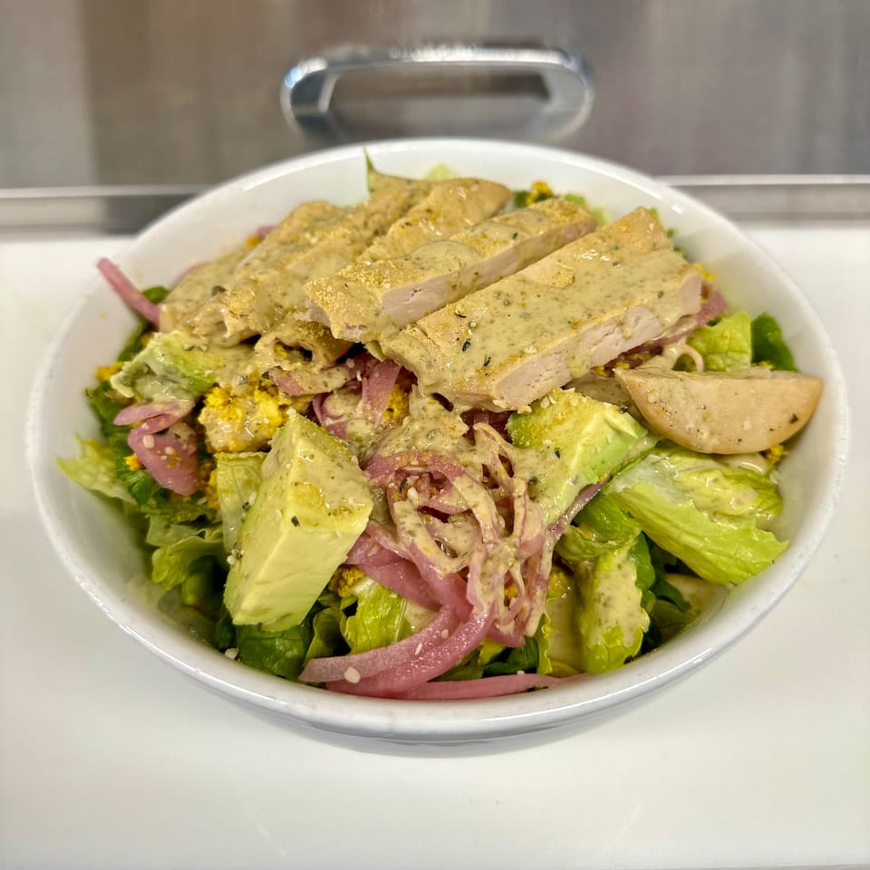 Vegan chicken salad with lettuce, avocado, pickled onions, and creamy dressing in a white bowl.