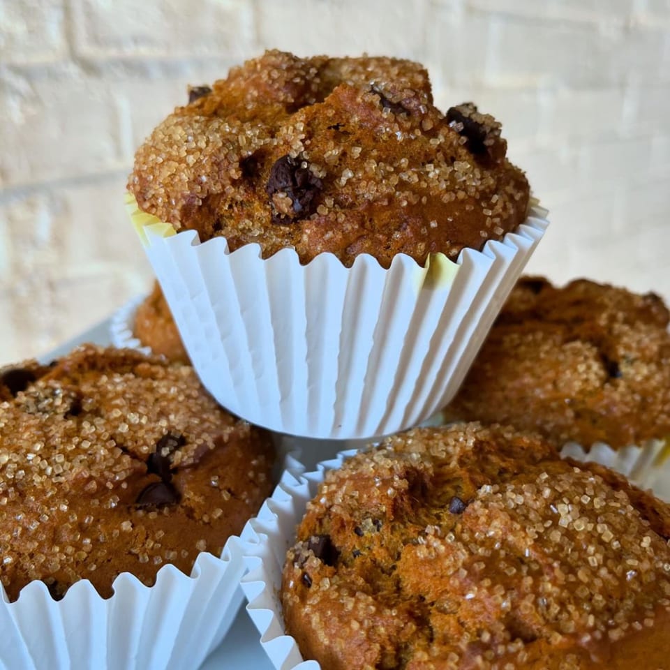 Close-up of vegan chocolate chip muffins with sparkling sugar tops, in white paper liners.