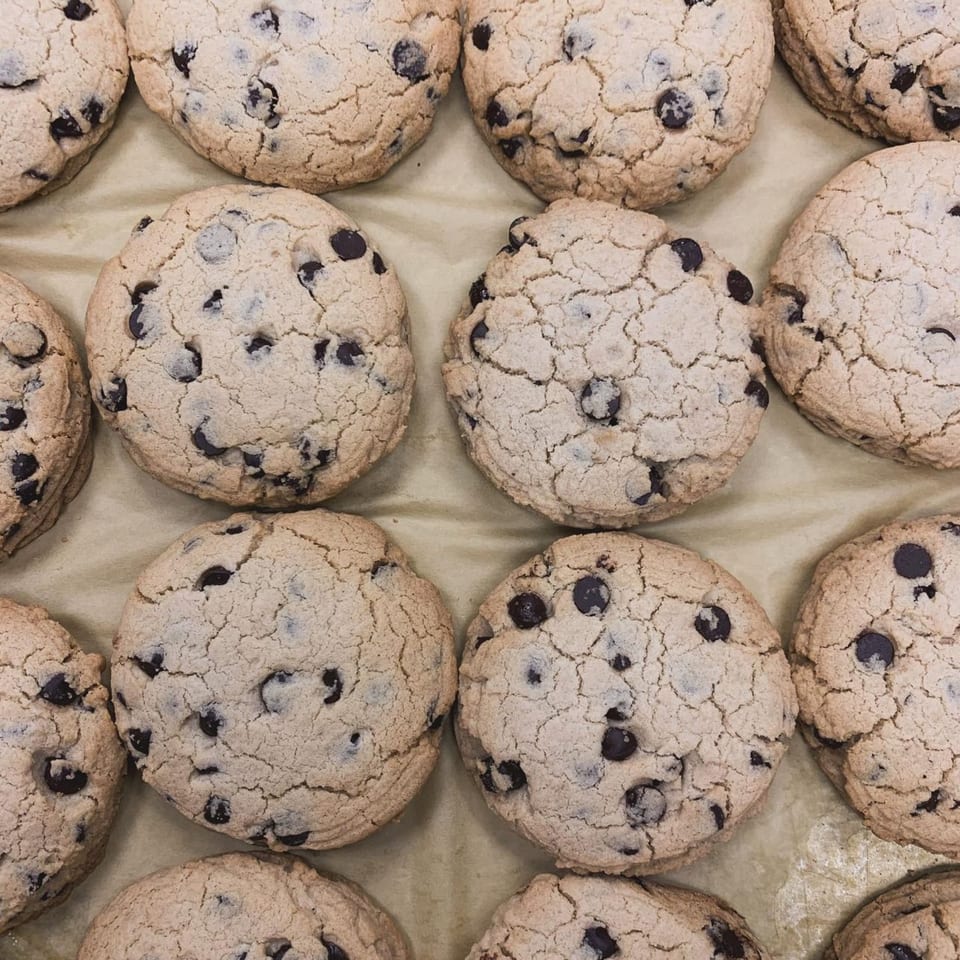 Close-up of several vegan chocolate chip cookies with cracked tops on a light brown surface.
