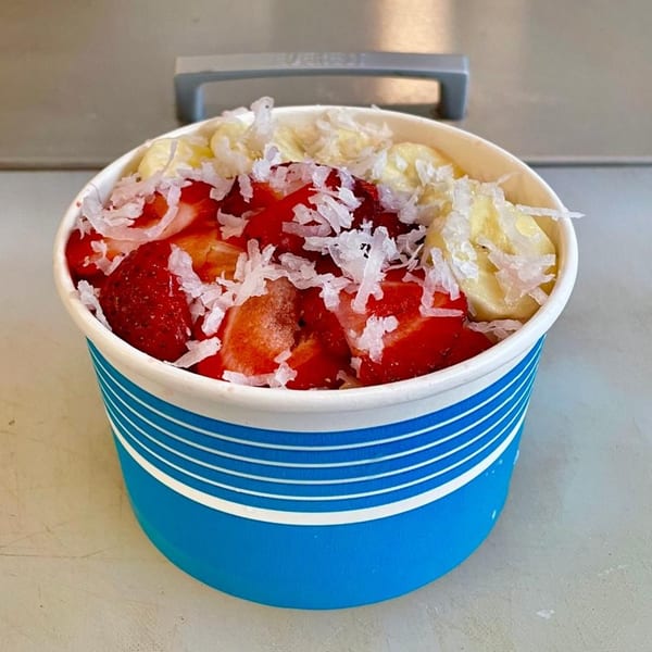 Vegan acai bowl from PB+J Bar, topped with strawberries, bananas, and shredded coconut.