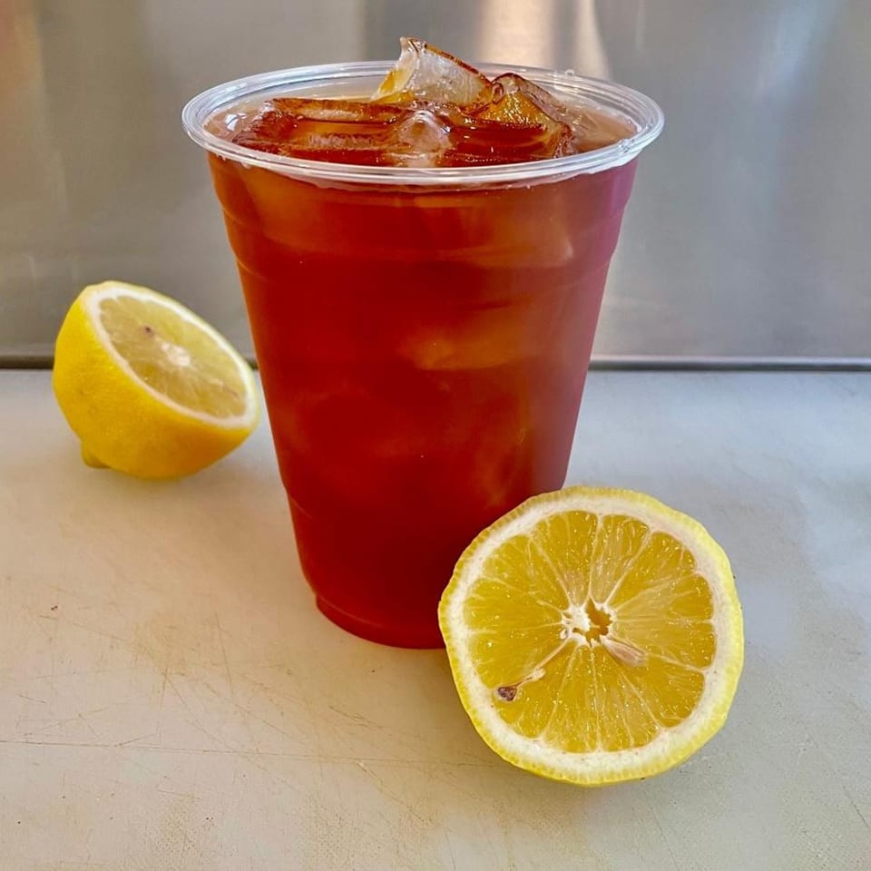 Iced tea in a plastic cup with two lemon halves on a white surface.